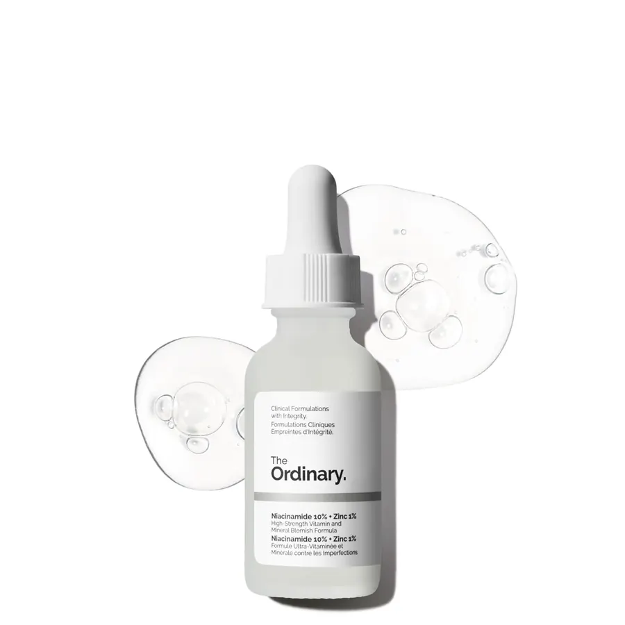 Small dropper bottle of The Ordinary Niacinamide serum held between two fingers beside a bathroom sink