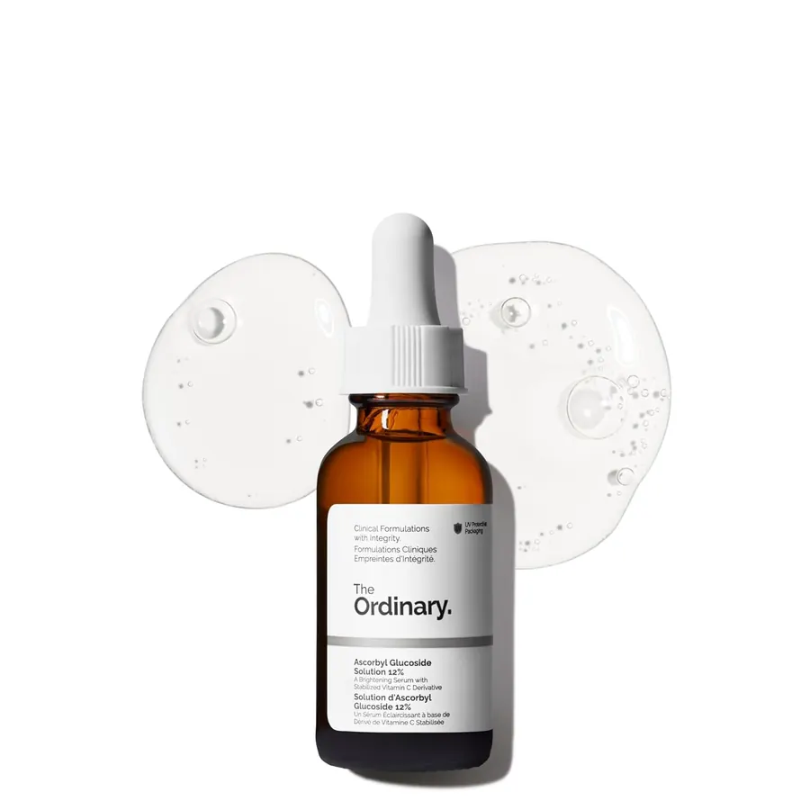 Close-up of a few drops of clear serum on fingertips above an open bottle of The Ordinary Ascorbyl Glucoside Solution